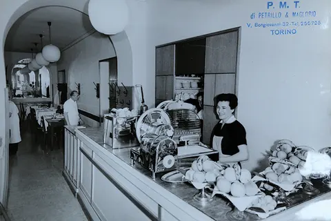 Foto in bianco e nero di una bottega di Torino col banco e le affettatrici, e l’insegna P.M.T.